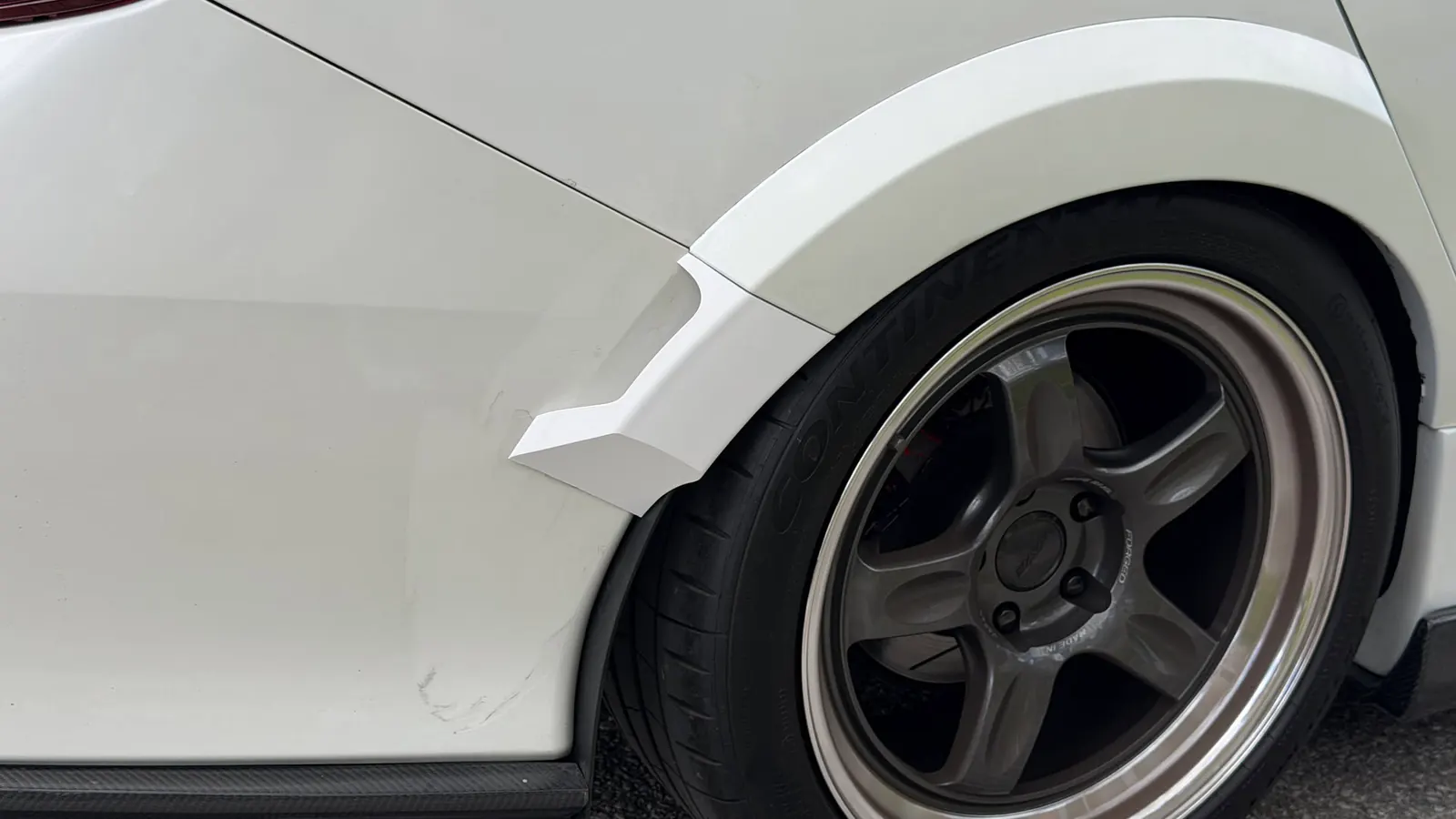 White winglet fitted behind the rear wheel of a white Honda Civic with bronze five-spoke wheels