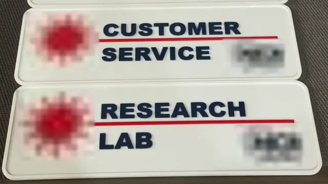 Two white 3D-printed room signs with raised navy lettering reading Customer Service and Research Lab, a red line under each name; logos blurred