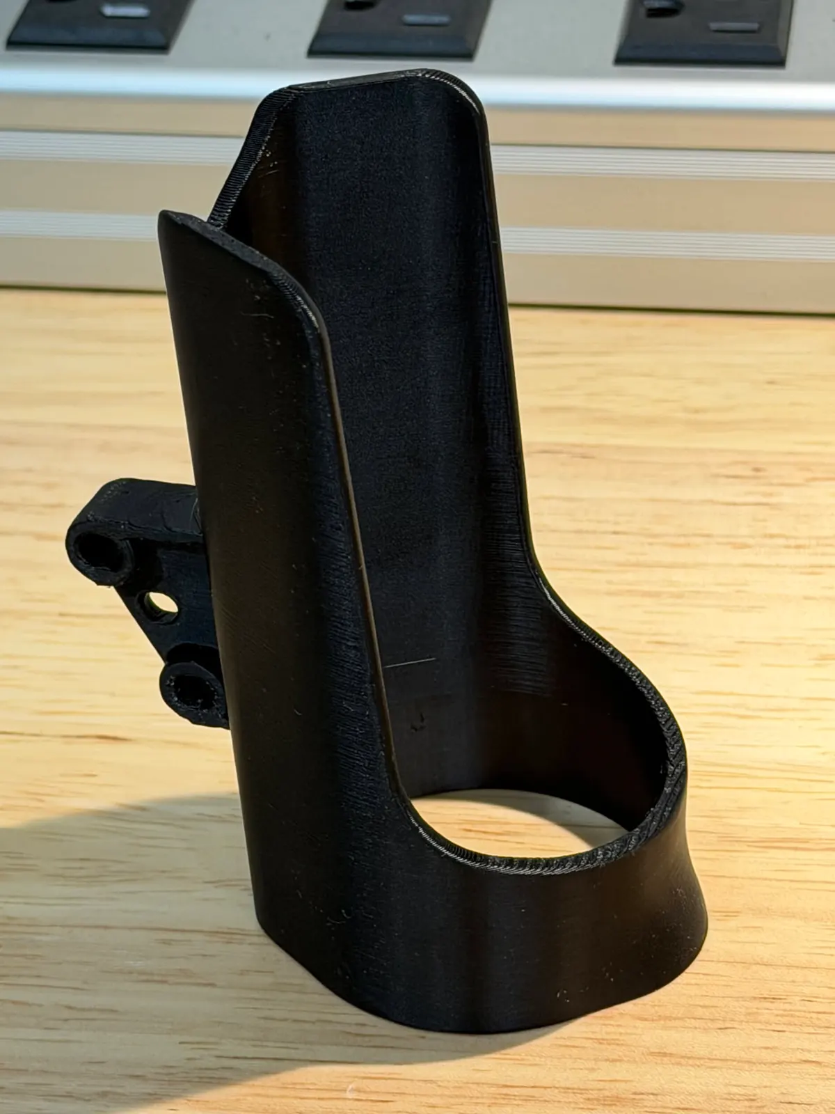 Black holder with a tall curved back, an open ring at the base and a mounting tab on its side